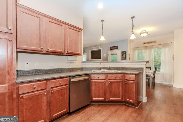 kitchen featuring dishwasher, a sink, dark countertops, light wood-type flooring, and a peninsula