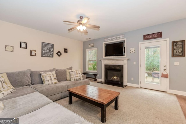 living room with light carpet, baseboards, a ceiling fan, and a glass covered fireplace