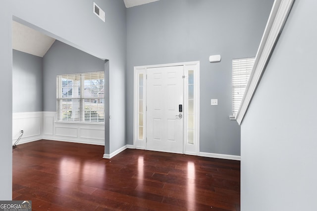 foyer entrance with visible vents, a decorative wall, wainscoting, vaulted ceiling, and wood finished floors