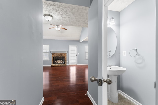 bathroom featuring a ceiling fan, baseboards, wood finished floors, and a stone fireplace