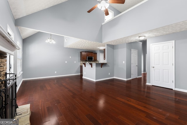 unfurnished living room with baseboards, wood-type flooring, a stone fireplace, high vaulted ceiling, and ceiling fan with notable chandelier