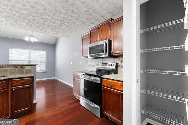 kitchen with dark wood-style floors, decorative backsplash, appliances with stainless steel finishes, a chandelier, and baseboards