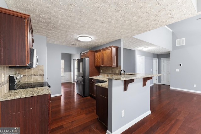 kitchen with dark wood-style flooring, stainless steel appliances, visible vents, a peninsula, and a kitchen breakfast bar