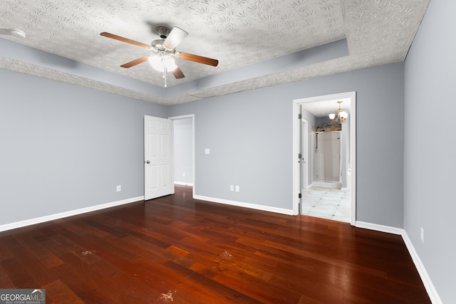 unfurnished bedroom with a tray ceiling, wood-type flooring, a textured ceiling, ensuite bath, and baseboards