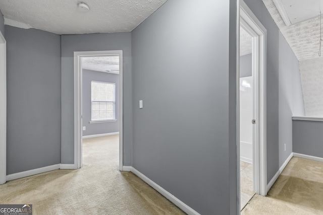 hallway featuring a textured ceiling, carpet, attic access, and baseboards