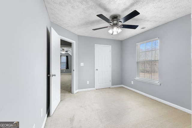 unfurnished bedroom with baseboards, visible vents, a textured ceiling, and light colored carpet