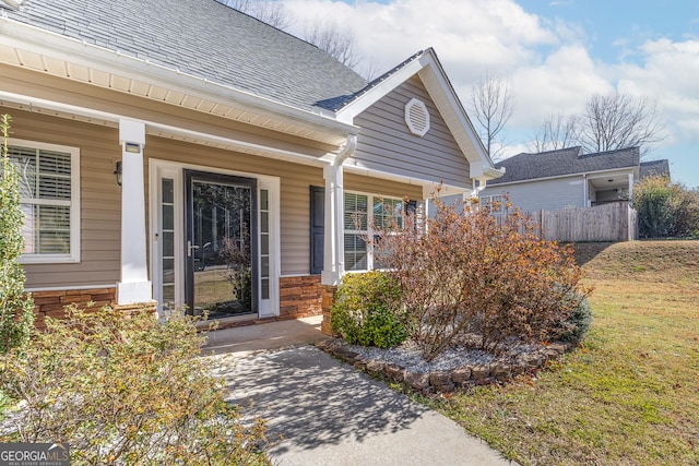 entrance to property with covered porch, fence, and roof with shingles