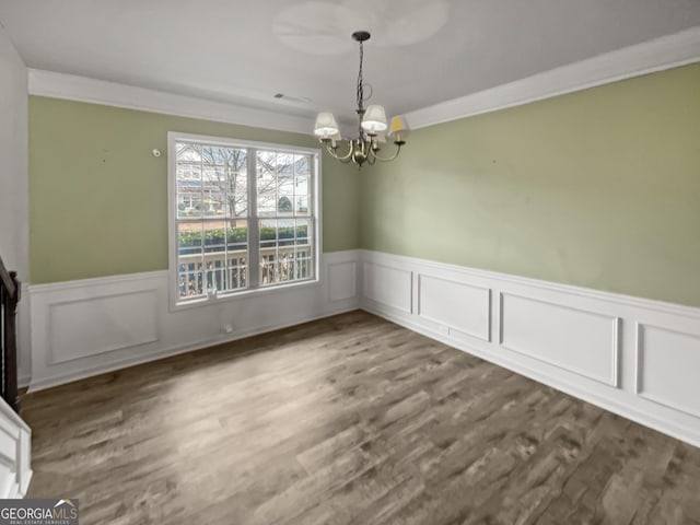 unfurnished dining area featuring a wainscoted wall, a chandelier, dark wood finished floors, and crown molding