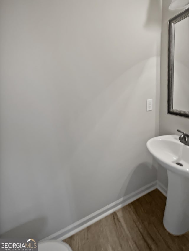 half bath featuring a sink, baseboards, and wood finished floors