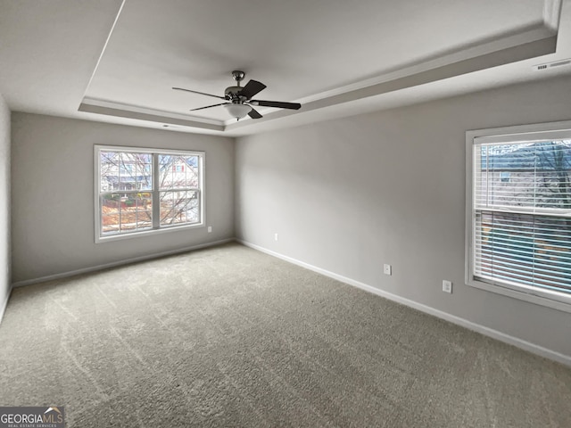 carpeted empty room with visible vents, a raised ceiling, a ceiling fan, and baseboards