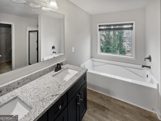 full bathroom with double vanity, wood finished floors, a sink, and a bath