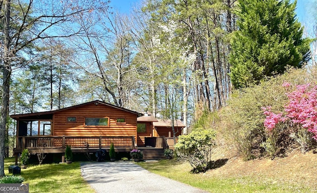 cabin featuring a wooden deck and a front yard
