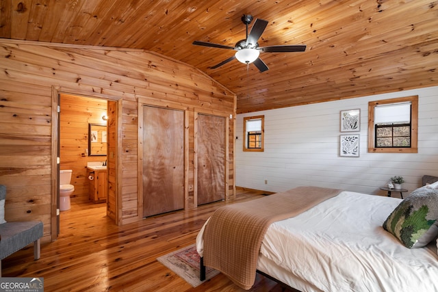 bedroom featuring light wood-style floors, connected bathroom, vaulted ceiling, wood ceiling, and wooden walls