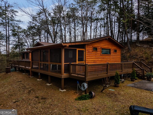 rear view of house featuring a sunroom, log veneer siding, and a deck