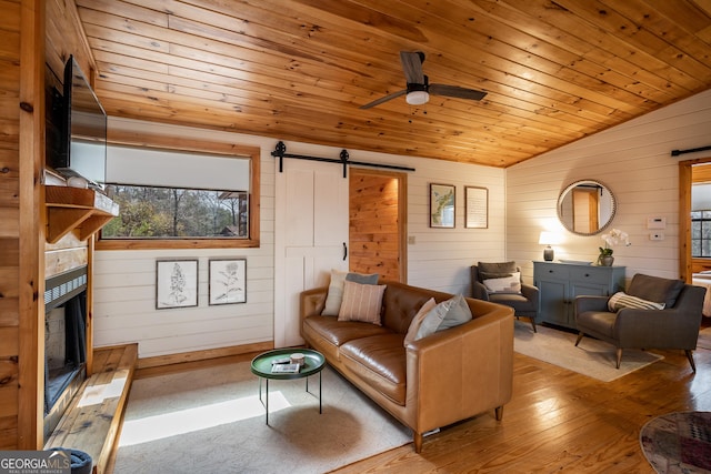 living room with a barn door, a ceiling fan, wood ceiling, wood walls, and lofted ceiling