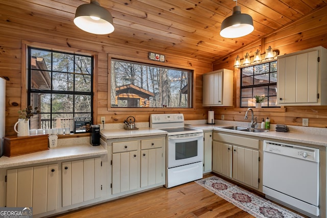 kitchen featuring a sink, wood walls, light countertops, and white appliances