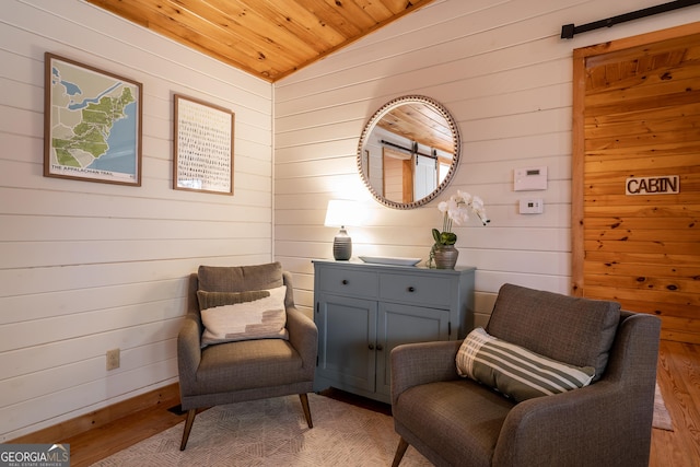 sitting room with baseboards, light wood-type flooring, wooden walls, lofted ceiling, and wooden ceiling