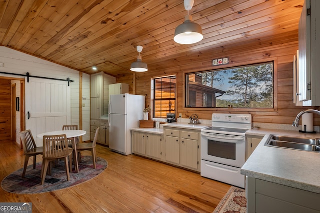 kitchen featuring a sink, wood walls, white appliances, and a barn door