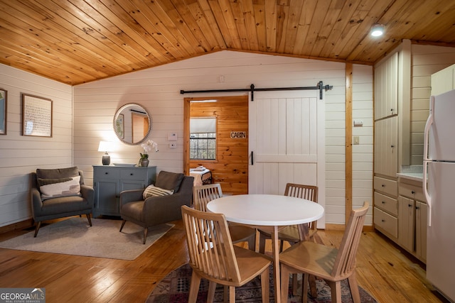 dining area with a barn door, light wood-style floors, wood ceiling, wooden walls, and vaulted ceiling