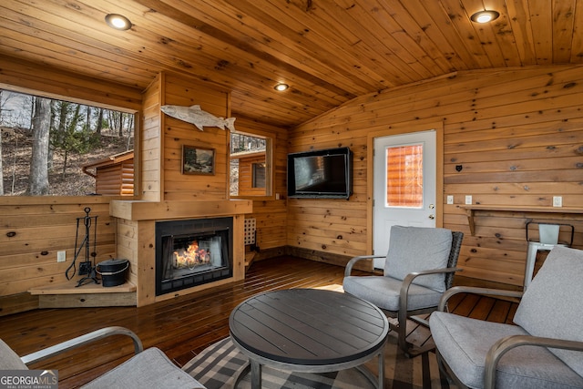 living area featuring recessed lighting, wood walls, hardwood / wood-style floors, a glass covered fireplace, and lofted ceiling
