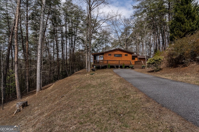 rustic home with aphalt driveway, a wooden deck, a front lawn, and log veneer siding