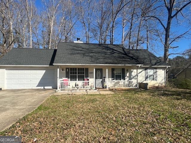 view of front facade featuring a porch, an attached garage, central AC, concrete driveway, and a front yard