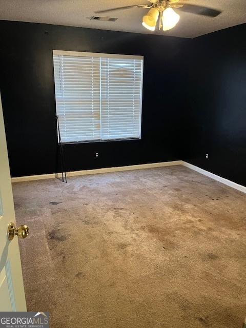 unfurnished room featuring carpet floors, ceiling fan, visible vents, and baseboards