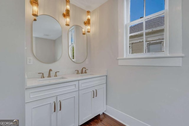 full bathroom with double vanity, wood finished floors, a sink, and baseboards