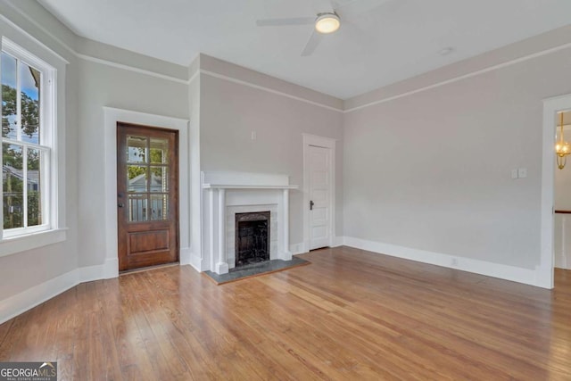 unfurnished living room with a fireplace with raised hearth, wood finished floors, and baseboards