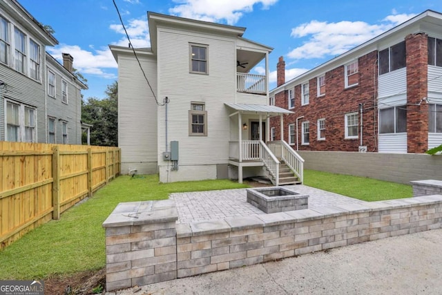 rear view of property with a balcony, a fire pit, fence, a ceiling fan, and a lawn