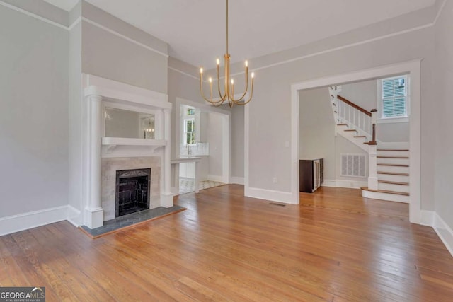 unfurnished living room featuring visible vents, a fireplace with raised hearth, stairway, wood finished floors, and baseboards