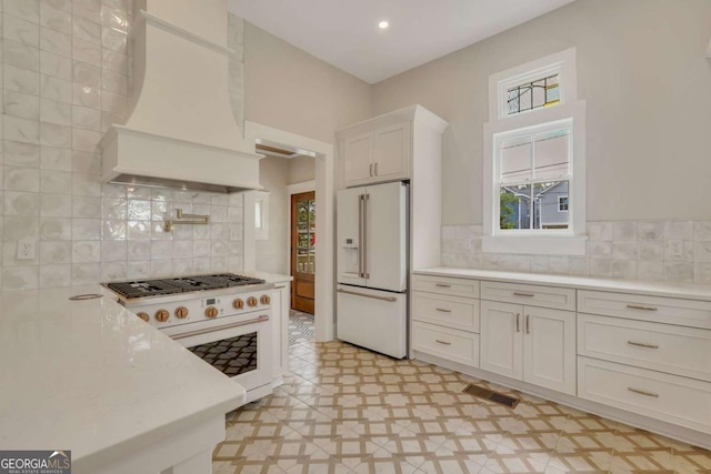 kitchen featuring high end white refrigerator, visible vents, custom exhaust hood, light countertops, and light floors