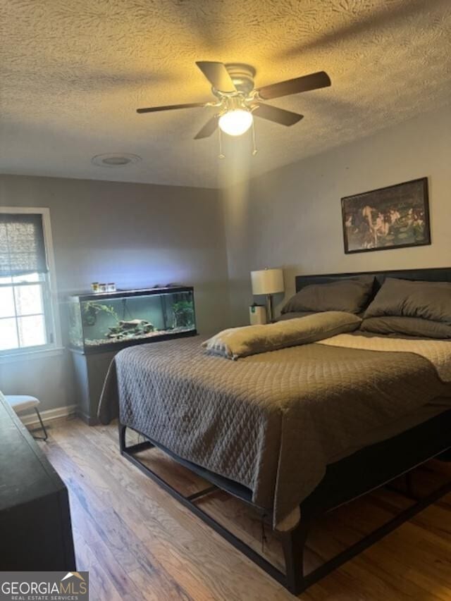 bedroom with a ceiling fan, wood finished floors, and a textured ceiling