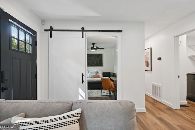 living room with a barn door, wood finished floors, visible vents, and baseboards