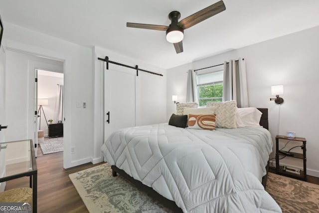 bedroom with a barn door, baseboards, ceiling fan, and dark wood-style flooring