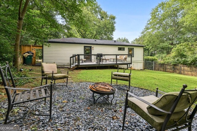 back of house with a deck, a fenced backyard, a lawn, and a fire pit