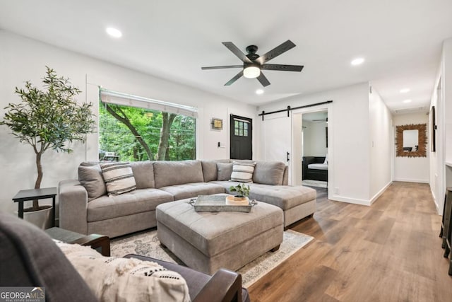 living room with a ceiling fan, a barn door, light wood-style flooring, and recessed lighting