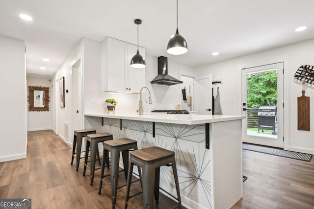 kitchen with light wood finished floors, light countertops, and wall chimney exhaust hood