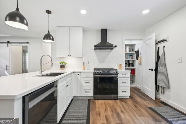 kitchen featuring stainless steel gas range oven, a sink, a barn door, wall chimney range hood, and dishwasher