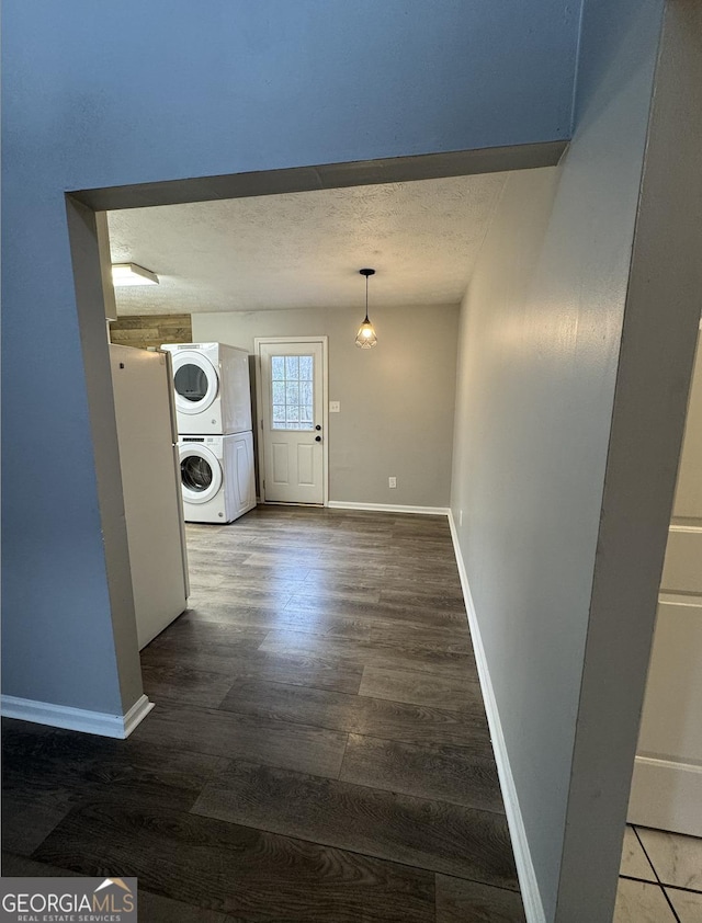 washroom with laundry area, baseboards, stacked washer / dryer, wood finished floors, and a textured ceiling