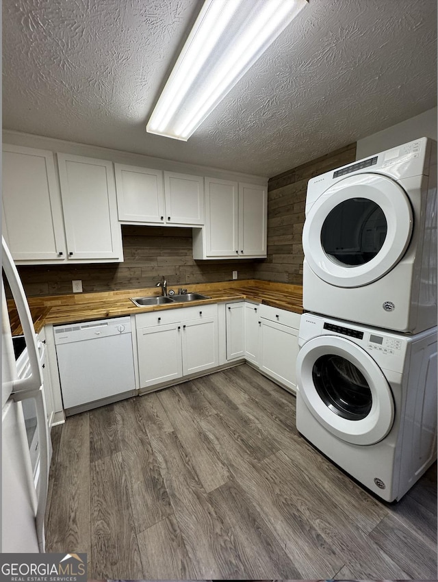 clothes washing area with laundry area, dark wood-type flooring, a textured ceiling, stacked washing maching and dryer, and a sink