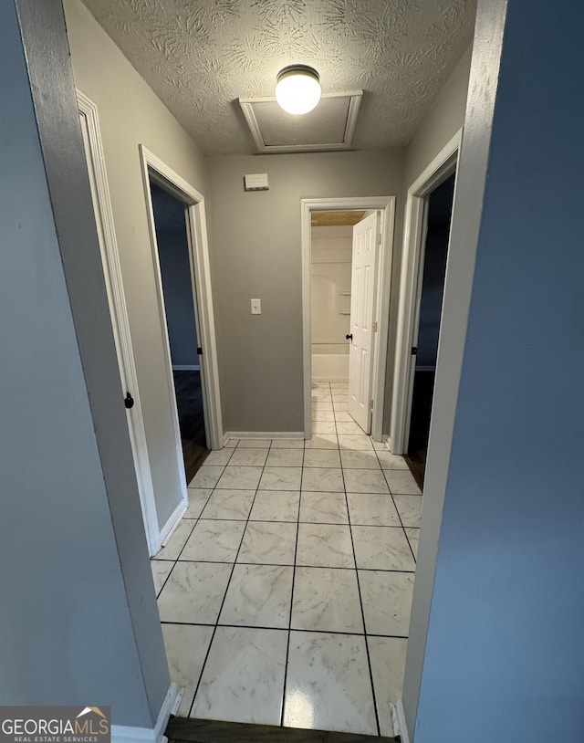 corridor featuring marble finish floor, attic access, baseboards, and a textured ceiling