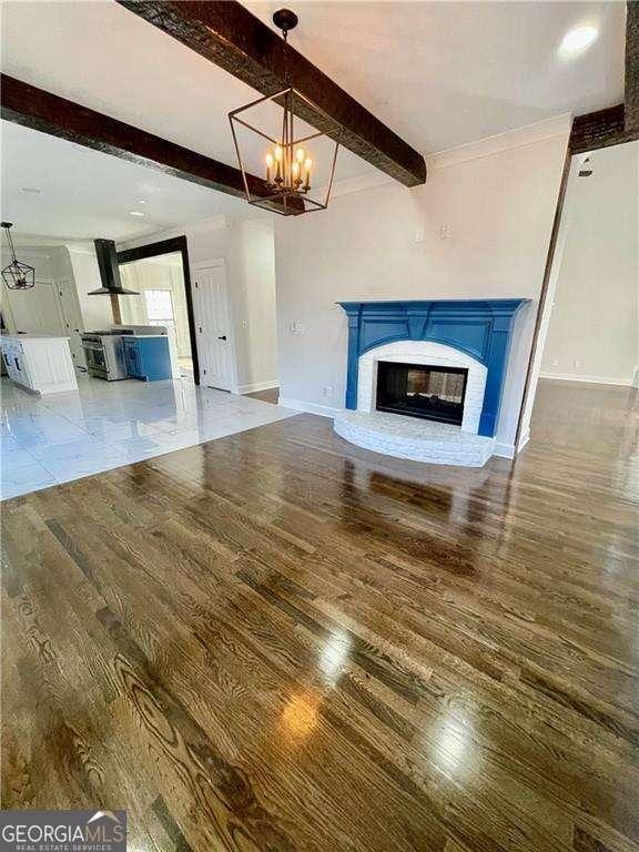 unfurnished living room featuring baseboards, wood finished floors, beamed ceiling, an inviting chandelier, and a brick fireplace