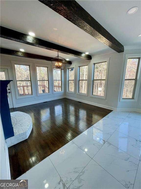 unfurnished living room featuring marble finish floor, an inviting chandelier, beam ceiling, and baseboards