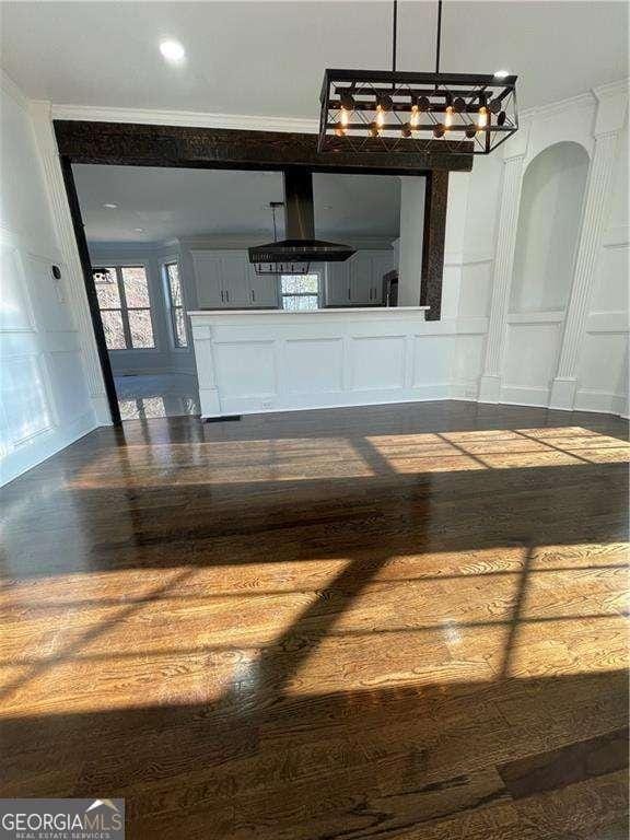 unfurnished living room featuring arched walkways, crown molding, dark wood finished floors, and a decorative wall