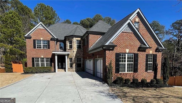 traditional home with driveway, stone siding, an attached garage, fence, and brick siding