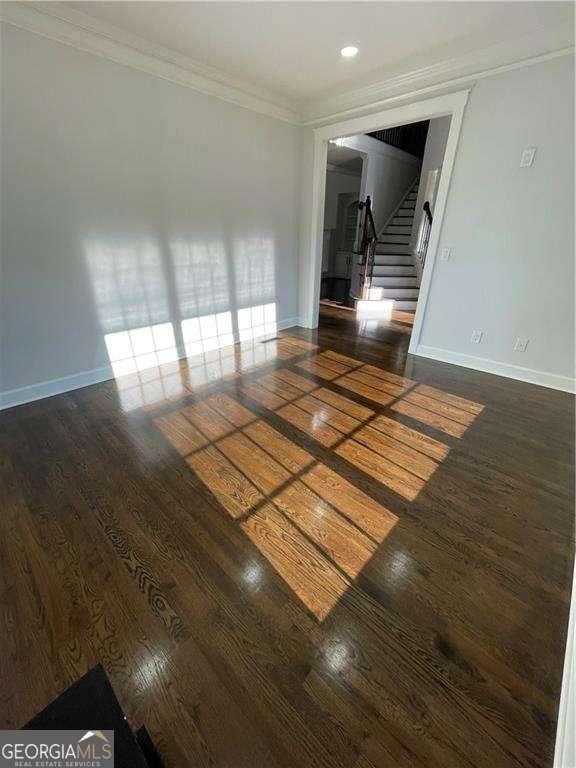 spare room with stairs, ornamental molding, wood finished floors, and baseboards