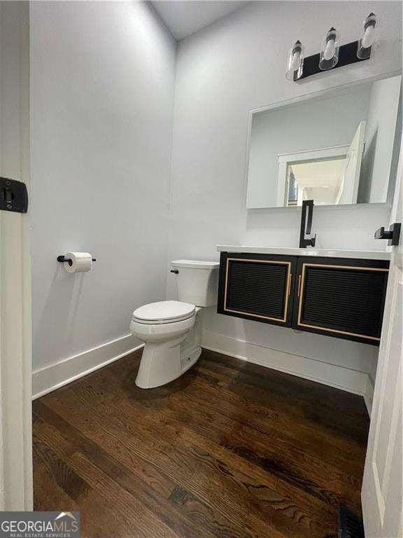 bathroom featuring toilet, baseboards, wood finished floors, and vanity