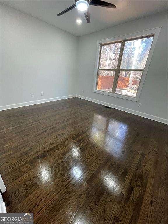 spare room featuring baseboards, dark wood finished floors, and a ceiling fan