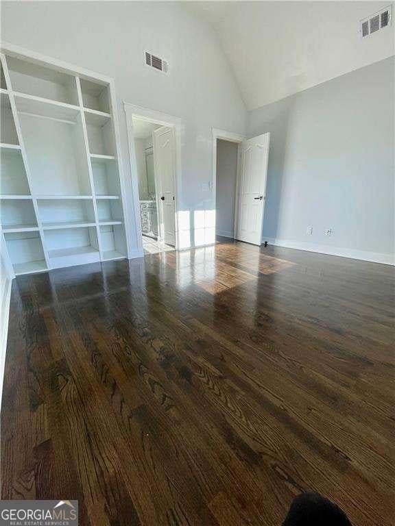 interior space featuring high vaulted ceiling, baseboards, visible vents, and wood finished floors